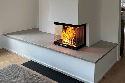 Moderner Eckkamin mit Glasfront und sichtbarem Feuer